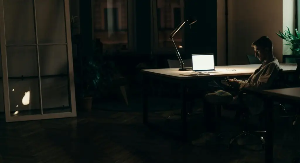 A man using his laptop in a dimly lit office at night, highlighting a dedicated work environment.