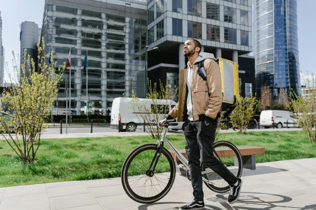 Cyclist with delivery backpack walking bike in Warsaw's modern urban setting.