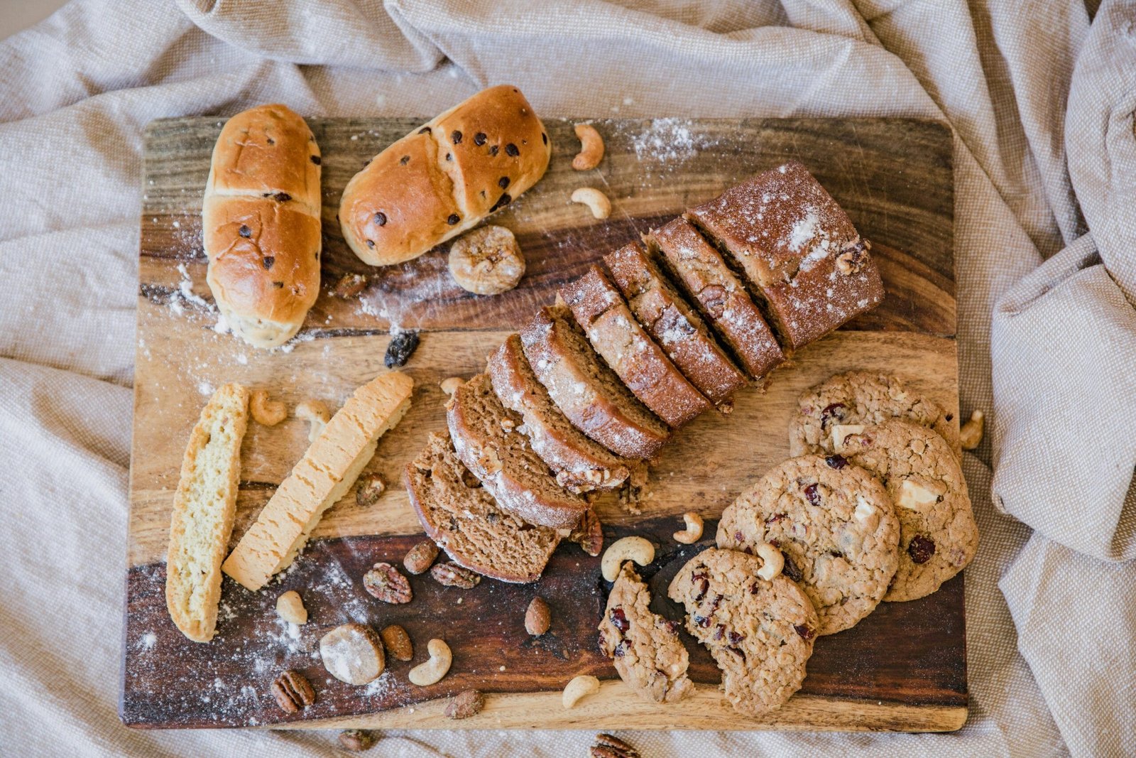 Top view of assorted baked goods including bread, cookies, and nuts on a wooden chopping board.