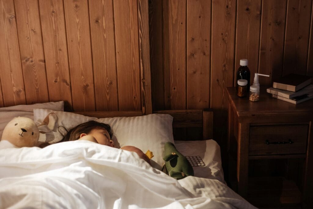 Child peacefully sleeping in a cozy wooden bedroom with toys and medicines by the bedside.